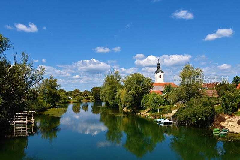 在斯洛文尼亚Dolenjska的Kostanjevica na Krki，可以看到Krka河，水中的天空和树木的倒影，教堂的塔从树叶中升起